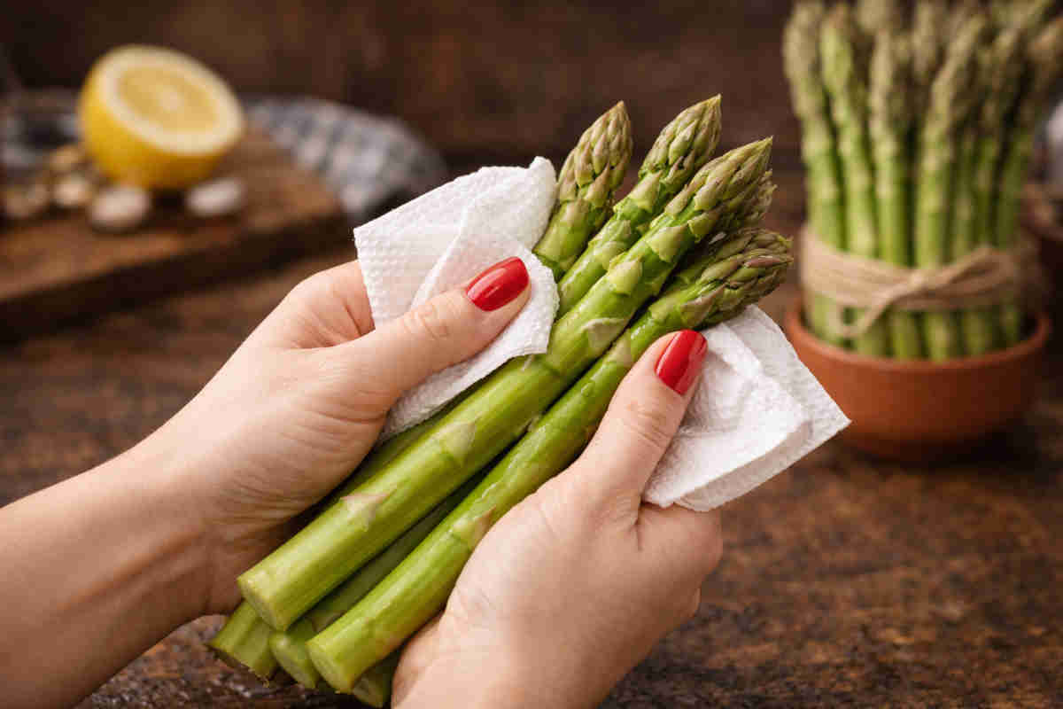 Mani femminili con smalto rosso che puliscono degli asparagi