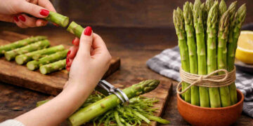 Mani femminili con smalto rosso che puliscono degli asparagi