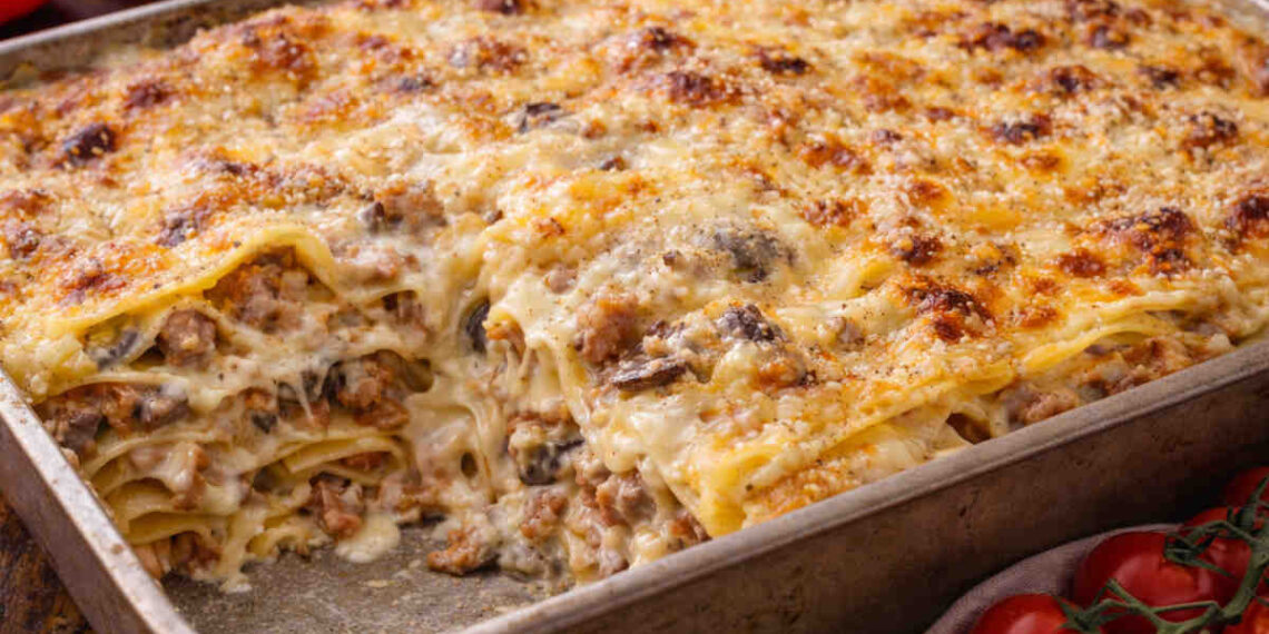 Teglia da forno in acciaio con all'interno una lasagna con funghi e salsiccia