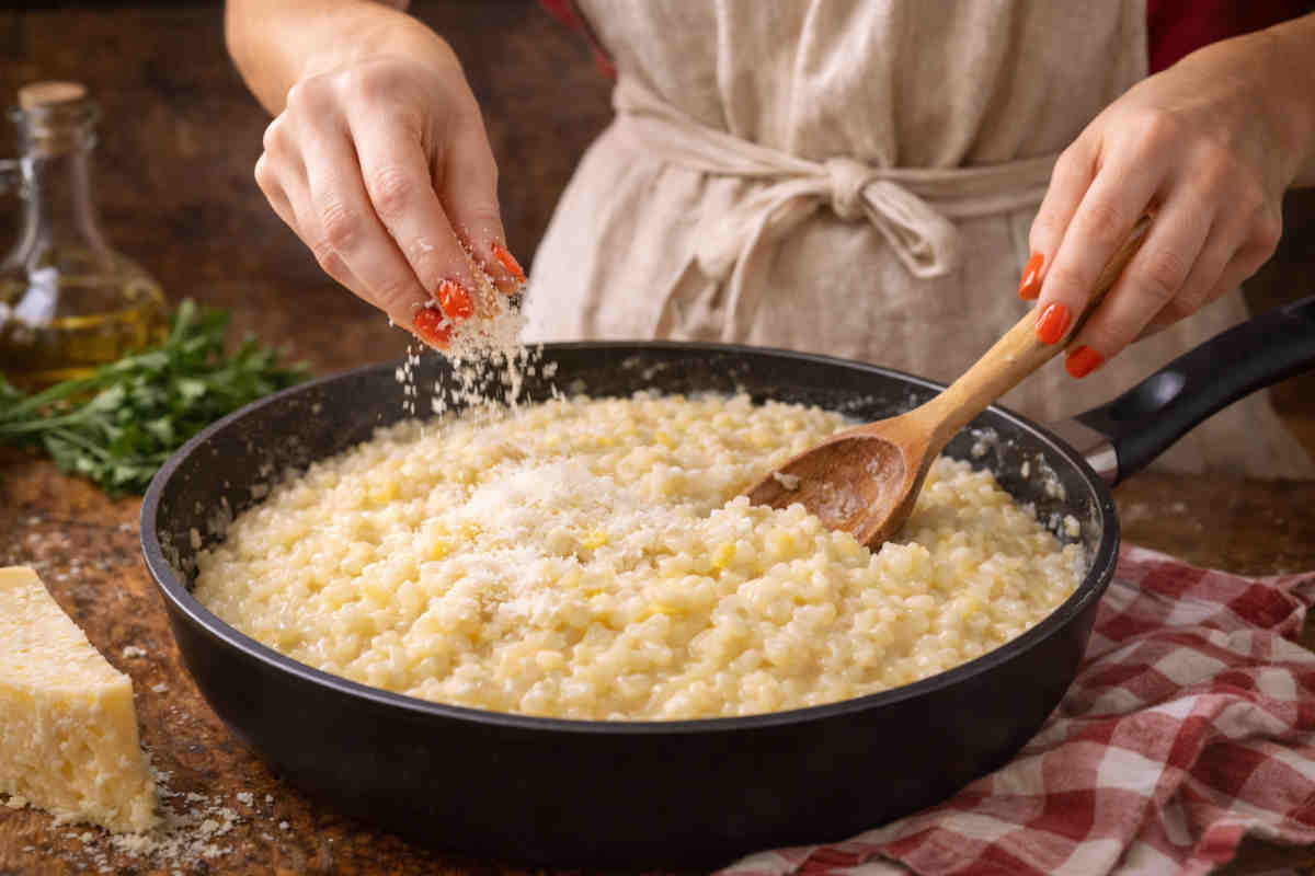 Donna in cucina che sta mantecando il risotto con del formaggio grattugiato
